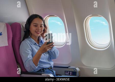 Femme asiatique écoutant de la musique et utilisant un smartphone dans l'avion Banque D'Images