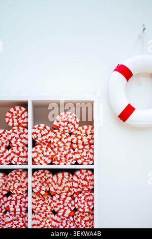 Étagères remplies de serviettes de plage rayées orange et blanches soigneusement roulées avec une bouée de sauvetage à proximité. Banque D'Images