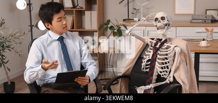 jeune homme d'affaires interviewant collègue squelette dans le bureau, concept de recrutement drôle avec candidat vide en costume formel et cravate, lieu de travail humoristique Banque D'Images