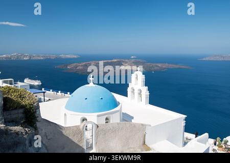 Église des trois cloches de Fira avec Blue Dome et clocher surplombant l'île volcanique de Caldera et la mer d'Aegeam, Santorin Banque D'Images