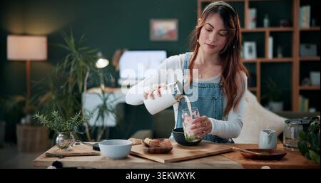 Bien-être, verser et femme avec matcha latte pour la nutrition, la boisson diététique ou un mode de vie sain à la maison. Personne, thé vert et lait dans le verre à la cuisine pour Banque D'Images