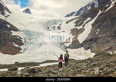 Troms, Norvège - 05.07.2020 : aventuriers debout sur un terrain rocheux surplombant un vaste glacier glacé niché dans des montagnes escarpées et enneigées Banque D'Images