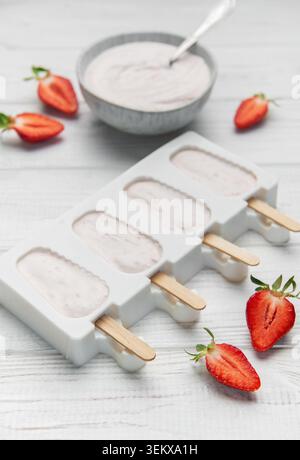 Popsicles au yaourt aux fraises dans un moule avec des baies fraîches et du yaourt crémeux sur une table en bois Banque D'Images