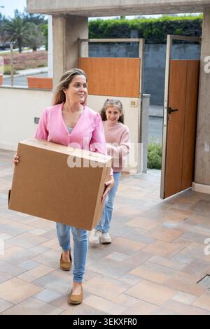 Mère et fille transportant des boîtes en carton tout en emménageant dans une nouvelle maison. Concept de déménagement familial montrant le travail d'équipe, le jour du déménagement, le nouveau départ, le nouveau b Banque D'Images