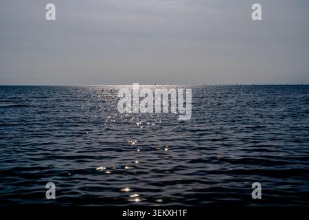 Surface de la mer calme avec des reflets de la lumière du soleil sous ciel brumeux près de l'horizon. Convient pour les voyages, la mer, la nature, le littoral et les thèmes de plein air paisibles. Banque D'Images