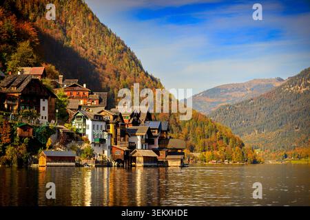 Hallstatt, Autriche - 20.10.2021 : maisons traditionnelles en bois reflétant dans le calme Hallstätter voir sous les arbres d'automne colorés et les montagnes escarpées Banque D'Images