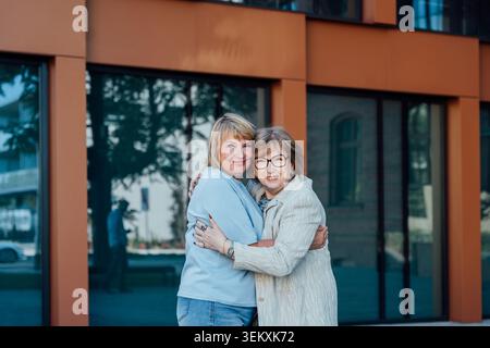 Femme d'âge moyen souriante et ami senior se serrant dans la cour de la ville Banque D'Images