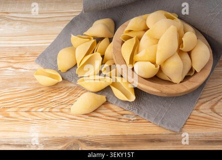 Pâtes conchiglioni crues dans un bol en bois. Nouilles conchiglies sèches en forme de coquille, gros macaronis italiens, pâtes de blé dur sur fond blanc Banque D'Images