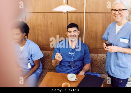 Portrait en grand angle d'un jeune infirmier souriant assis à table dans la cafétéria de l'hôpital pendant la pause café Banque D'Images
