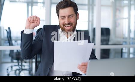 Motivé homme d'affaires caucasien d'âge moyen heureux avec des documents de bons résultats danse réjouissant contrat de conclusion de travail avec de la musique en compagnie Banque D'Images