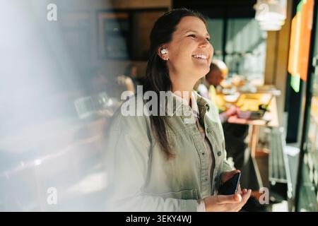 Femme d'affaires heureuse regardant loin tout en parlant à l'appel à l'aide d'écouteurs sans fil au bureau Banque D'Images