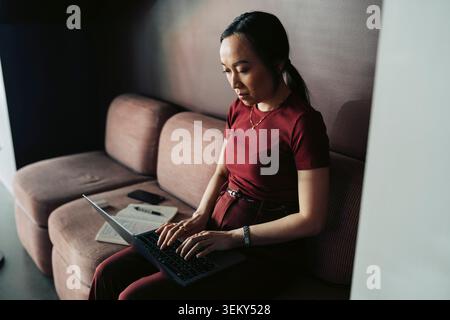 Femme d'affaires travaillant sur ordinateur portable tout en étant assis sur le canapé à l'espace de travail moderne Banque D'Images