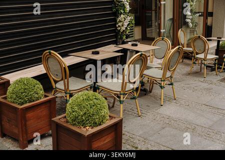 Espace de sièges extérieur vide d'un café avec des tables, des chaises et des plantes décoratives. Concept d'hospitalité et de style de vie urbain. Banque D'Images