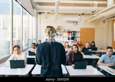 Vue arrière d'une femme professeure enseignant des élèves du premier cycle du secondaire en classe Banque D'Images