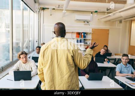 Vue arrière d'un professeur masculin enseignant des élèves en classe au collège Banque D'Images