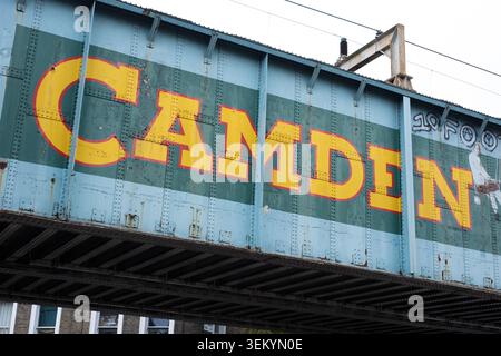 Vue rapprochée de la rue des emblématiques lettres typographiques peintes en jaune du panneau Camden sur une structure de pont ferroviaire en métal bleu, Londres Banque D'Images