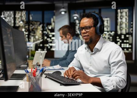 Développeur de logiciels écoutant de la musique au bureau, examinant les métriques du système, surveillant les tableaux de bord de performance. Société technologique expert INFORMATIQUE Wearing casque audio accordant des réseaux neuronaux à l'aide d'un ordinateur Banque D'Images