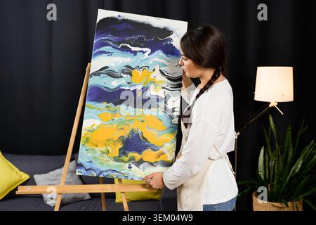 Jeune femme exprime son talent artistique à la maison tout en mettant en valeur une peinture vibrante. Banque D'Images