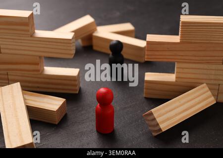 Mur en bois effondré fait de blocs et de figures humaines sur la table noire, gros plan. Surmonter les obstacles Banque D'Images