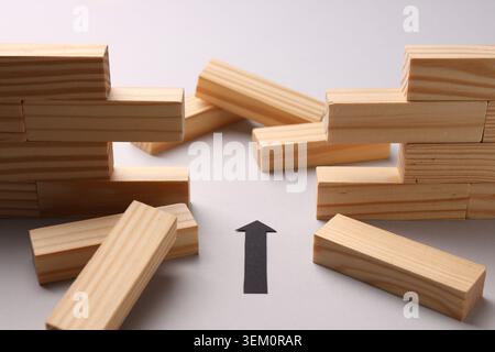 Mur en bois effondré fait de blocs et flèche de papier noir sur fond blanc, gros plan. Surmonter les obstacles Banque D'Images