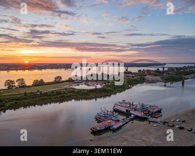 Vue aérienne du fleuve Mississippi au coucher du soleil avec des bateaux à quai, un parc avec piscine et le pont Hernando de Soto à Memphis, Tennessee. Banque D'Images