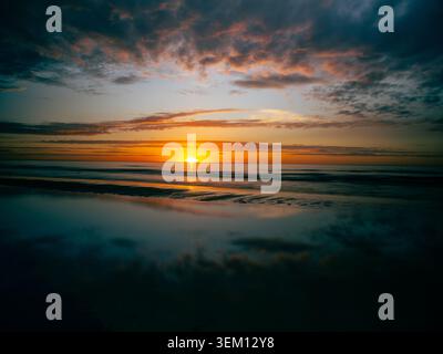 Coucher de soleil doré spectaculaire sur la mer Baltique avec des nuages vibrants et un reflet parfait de l'eau sur la plage de sable humide à Jurmala, Lettonie. Banque D'Images