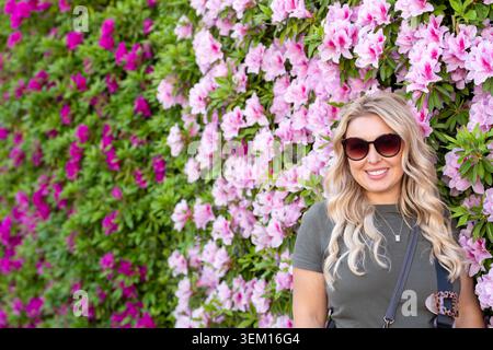 Femme blonde se tient devant un mur de fleurs roses, portrait Banque D'Images