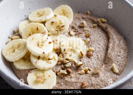 Bouillie de lin saine garnie de tranches de banane, de noix hachées et de graines dans un bol en céramique. Petit déjeuner nutritif avec des ingrédients naturels, gros plan Banque D'Images