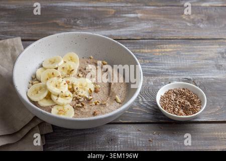 Bouillie de lin saine garnie de tranches de banane, de noix hachées et de graines dans un bol en céramique. Petit déjeuner nutritif avec des ingrédients naturels, copie Banque D'Images