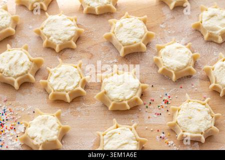 Beaucoup de biscuits au fromage italien cru avec garniture de zeste de citron préparés sur une surface farinée. Production de pâtisseries pardulas sardes traditionnelles à la maison Banque D'Images