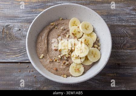 Bouillie de lin saine garnie de tranches de banane, de noix hachées et de graines dans un bol en céramique. Petit déjeuner nutritif avec des ingrédients naturels, vue de dessus Banque D'Images