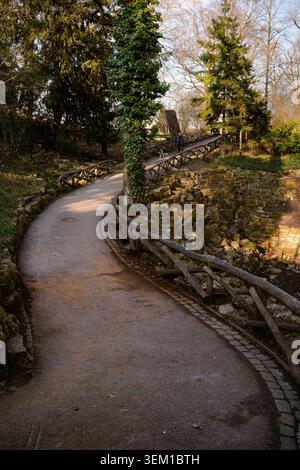 Un sentier sinueux bordé de balustrades en bois rustiques et de murs en pierre moussue dans une lumière naturelle chaude. Scène extérieure paisible avec une ligne de tête forte Banque D'Images