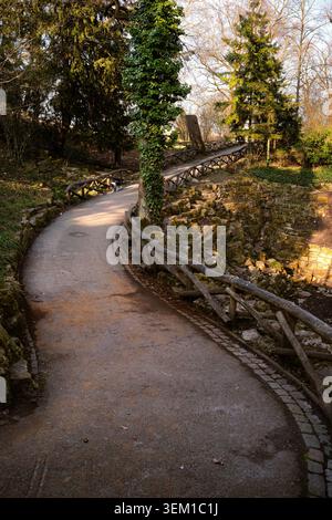 Un sentier sinueux de parc avec des garde-corps rustiques en bois, capturé dans la lumière naturelle chaude avec un petit chien marchant au loin. Scène extérieure paisible wi Banque D'Images