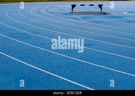 Piste de course bleue vide avec saut en eau steeplechase et marquage des voies dans un stade d'athlétisme extérieur. Banque D'Images