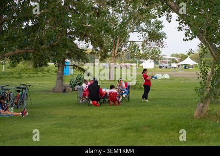 Un groupe de personnes ayant un pique-nique et se relaxant sur une pelouse verte dans un parc avec des vélos et des tentes en arrière-plan. 07.07.2023 - Calgary, Canada Banque D'Images