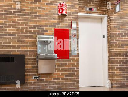 Une photo intérieure de haute qualité d'un couloir de campus universitaire avec un ascenseur moderne, une station de remplissage d'eau et une armoire extinctrice montée Banque D'Images
