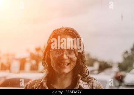 Femme lunettes de soleil rire jeune femme souriante avec les cheveux mouillés profitant d'une journée d'été ensoleillée à l'extérieur dans une ville urbaine Banque D'Images