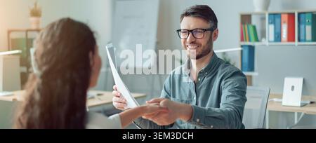 Souriant homme caucasien remettant le document à la femme au bureau, concept d'affaires Banque D'Images