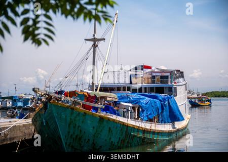 Makassar, Indonésie - 9 février 2024 : Bateau de charge en bois traditionnel amarré au port de Paotere, sa cargaison recouverte d'une bâche bleue. Banque D'Images