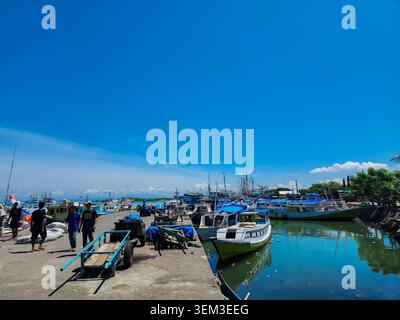 Makassar, Indonésie - 09 février 2024 : Des gens marchant le long du quai du port de Paotere à côté de charrettes à main et de bateaux traditionnels en bois. Banque D'Images