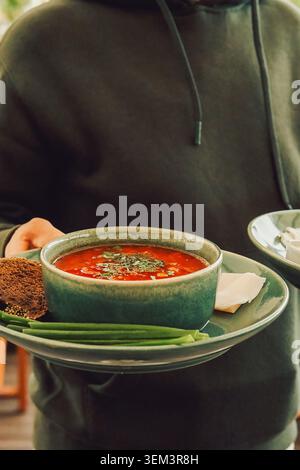 Soupe chaude servie avec du pain et des oignons verts dans un cadre décontracté pendant un après-midi ensoleillé. personne tient deux assiettes avec borsch et pain dans re Banque D'Images