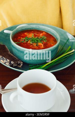 Soupe chaude et thé servis sur table avec des légumes verts frais et du pain dans un cadre confortable pendant la journée d'hiver. bol borsch sur la table près d'une tasse de thé. Gree frais Banque D'Images