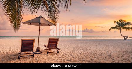 Deux chaises de plage sous un parasol sur du sable tropical à un coucher de soleil chaud avec des palmiers. Ciel rose mer. Couple romantique lune de miel voyage vacances bien-être Banque D'Images