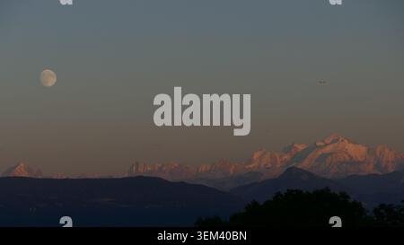 Vue aérienne du massif du Mont Blanc avec alpenglow sur les sommets enneigés et une pleine lune dans le ciel crépusculaire au-dessus de Chamonix, Auvergne-Rhône-Alpes, Banque D'Images
