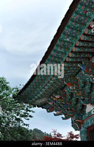 Gros plan d'avant-toit peint dancheong orné avec des motifs floraux et de volutes complexes en sarcelle, orange et bleu dans un temple bouddhiste, Odaesan, Corée du Sud Banque D'Images