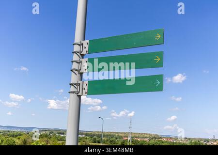 Une photo en extérieur de trois plaques de pointage de flèche directionnelle vierges en métal vert montées sur un lampadaire en acier public ou un poteau de service public contre un s bleu vif Banque D'Images