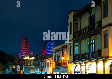 Bâtiments traditionnels en pierre avec balcons en bois à Icheri Sheher la nuit, avec des tours de flammes illuminées derrière. Bakou, Azerbaïdjan. Banque D'Images