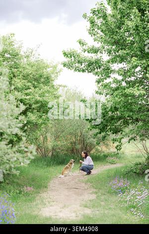 Femme souriante avec son chien sur un beau chemin forestier Banque D'Images