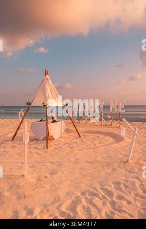 Proposition de mariage sur une plage de sable blanc, teepee avec table à manger et panneau de lettres, décoration romantique de fiançailles au bord de la mer en journée Banque D'Images
