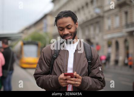 Le jeune homme noir vérifie le téléphone dans une rue de la ville Banque D'Images